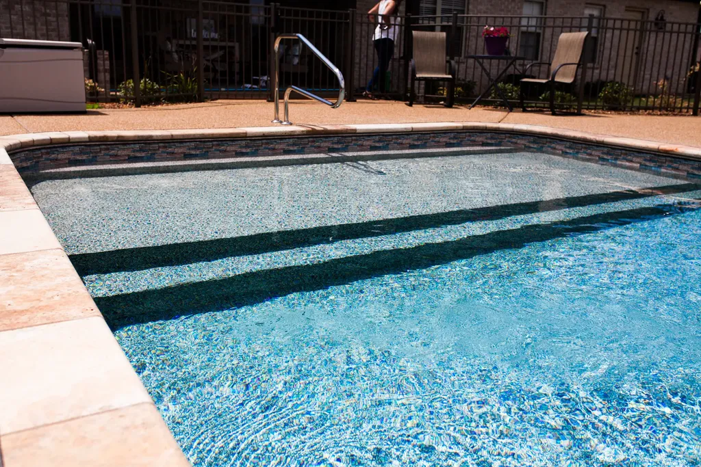 a photo of the shallow end of a Stone Mosaic Pool Liner Pattern pool with a rail in the middle and a tanning ledge and steps into a pool.